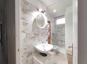 A modern bathroom with a marble wall, a round mirror, a white sink, and a shower area. - Beach 2 Large Balcones Quiet Rooms Wifi (Sitges)