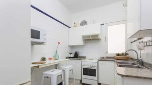 Pieni, käytännöllinen keittiö, jossa on valkoiset kaapit, mikroaaltouuni, liesi ja pesuallas.