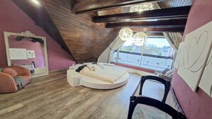 Une chambre avec un plafond en pente, un lit rond, une fenêtre donnant sur un beau paysage et une poussette.
