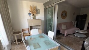 A dining area with a glass-top table, white chairs, a small side table, and a ceiling light fixture. - Charming two-bedroom apartment in La Motte-du-Couchant, 200 meters from the beaches (La Grande-Motte)