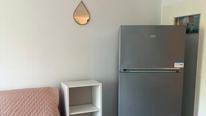 A small room with a bed, a white shelving unit, and a grey refrigerator. - Charming two-bedroom apartment in La Motte-du-Couchant, 200 meters from the beaches (La Grande-Motte)