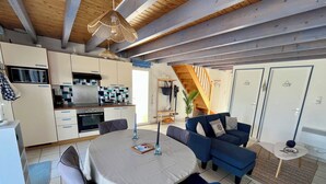 Ett modernt kök med vita skåp, ett matbord med stolar, en blå soffa och en trappa som leder till ett annat våningsplan.