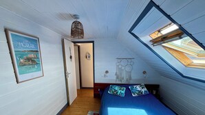 Ett sovrum med ett sluttande tak, en säng med blått sänglinne, en drömfångare som hänger på väggen och en inramad bild av ett kustlandskap.
