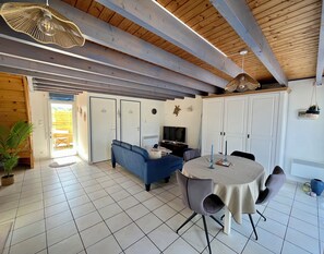 A room with a sofa, dining table, chairs, and a television. There are doors and a window.