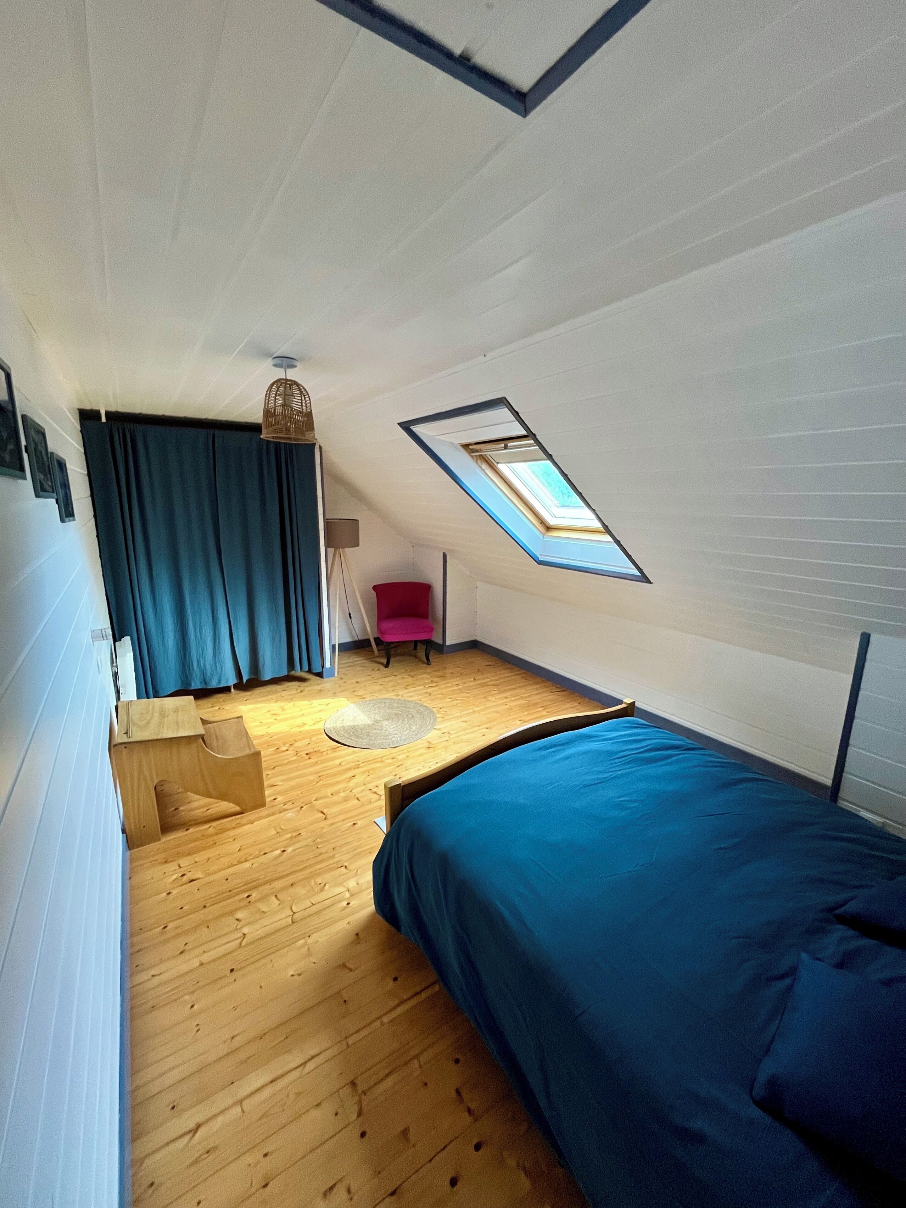 Een kamer met een schuine kap, dakraam, bed, bureau en stoel.