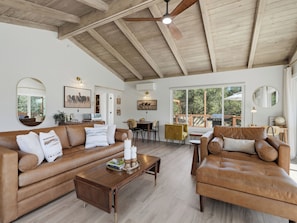 A spacious living room with a high ceiling, wooden beams, a large window, a dining area, and a cozy seating arrangement. - Private. Luxury. River House Retreat at Yosemite. Hot Tub. Outdoor Shower. Views (Coarsegold)