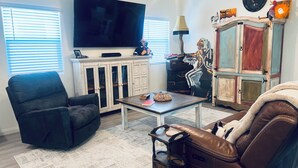 Ein Wohnzimmer mit schwarzem Ledersofa, einem braunen Ledersessel, einem weißen Schrank mit Glastüren, einem Flachbildfernseher und einer Lampe.