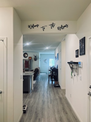 Um corredor com a placa 'Welcome to the Nelsons', uma área de refeições, um local para alimentação de animais de estimação e um bebedouro fixado na parede.