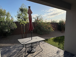 A patio with a table and an umbrella, surrounded by greenery and a brick wall.