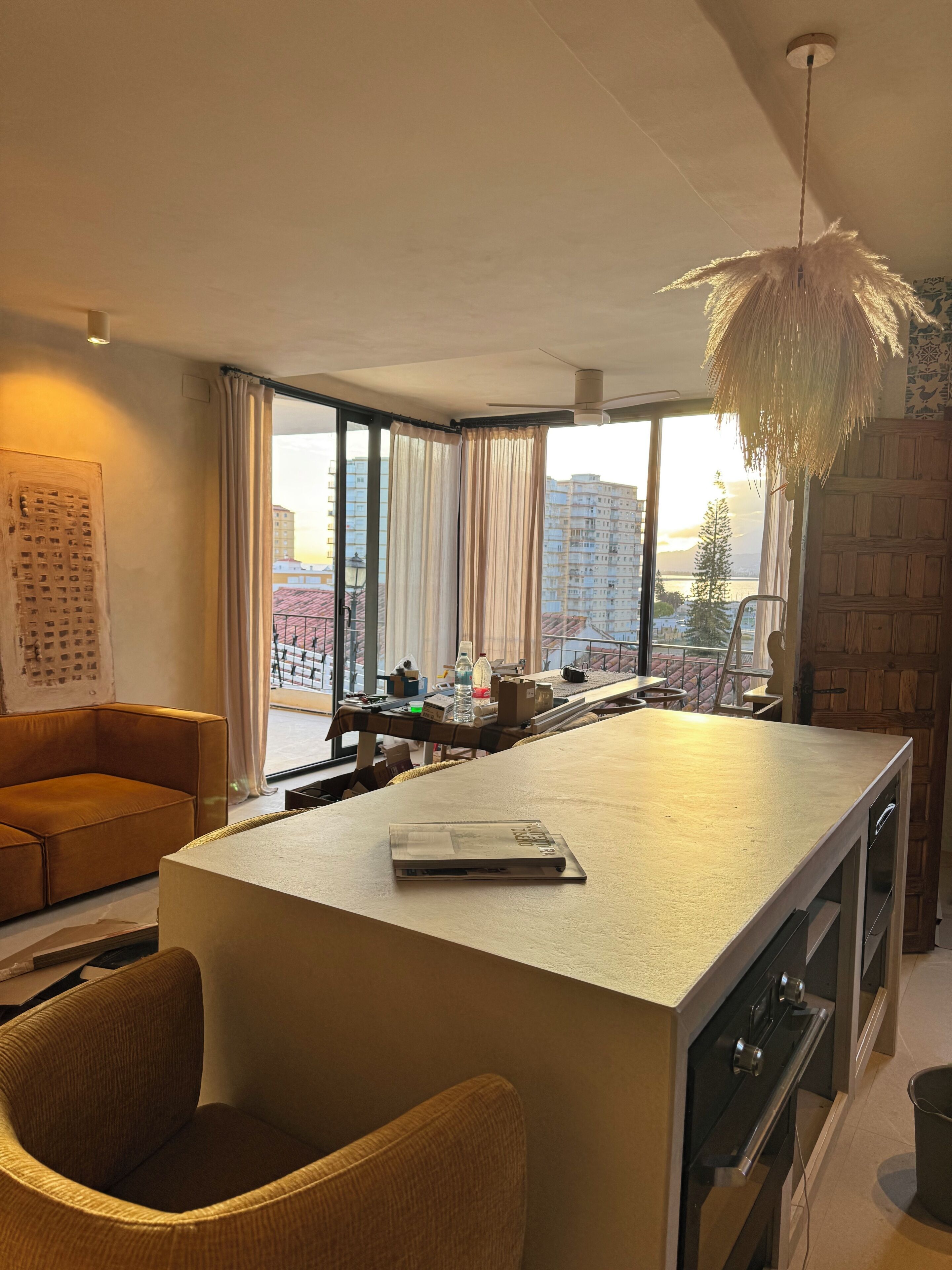 Une cuisine moderne dotée d’un grand îlot central, d’un coin repas avec un canapé et offrant une vue sur les bâtiments grâce à de grandes fenêtres.