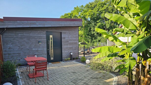 Un bâtiment moderne avec une porte sombre, une table et des chaises rouges, et un patio dallé.