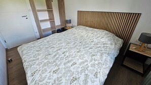 Une chambre à coucher comprenant un lit, une tête de lit en bois, une table de chevet avec une lampe et une armoire avec un miroir.