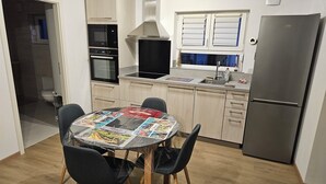 Une cuisine de taille réduite comprenant une table à manger, des chaises, un réfrigérateur et une fenêtre avec des stores.
