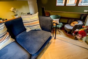 A room with a dark blue sofa, striped pillows, a green armchair, and a grey armchair with a cushion.