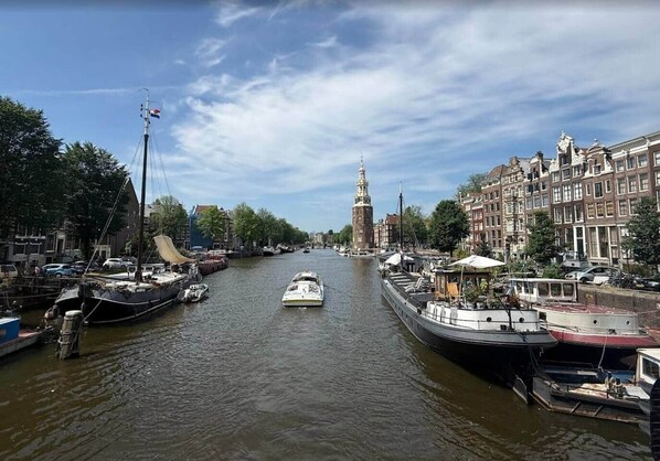 A canal with boats docked on both sides, a prominent tower in the distance, and buildings lining the waterway.