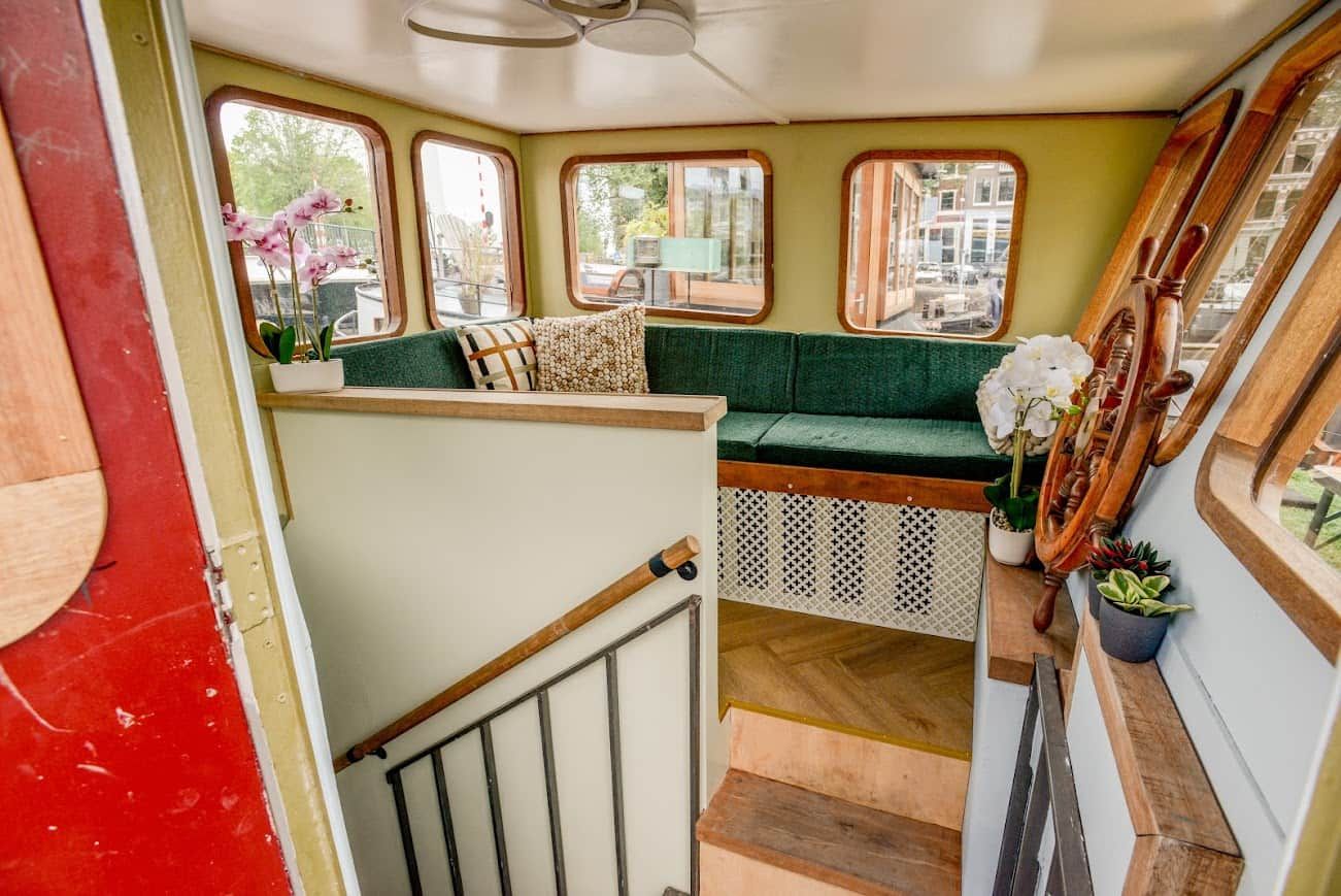 A cozy interior with a green cushioned bench, wooden railing, and potted plants.