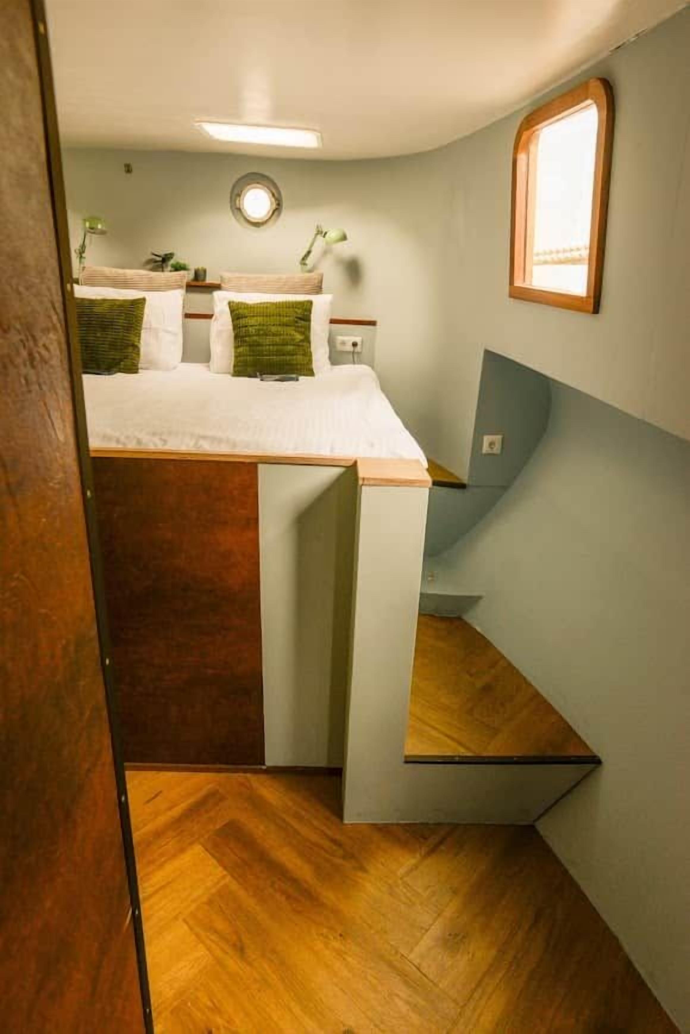 Un dormitorio con cama, mesita de noche, espejo y ventana.