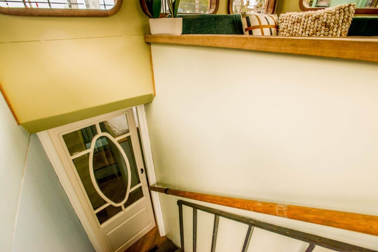 A staircase with a wooden handrail, a white door with a glass panel, and a shelf with decorative items.