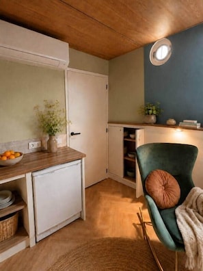 A compact kitchen with a refrigerator, a wooden countertop, a chair, and a small cabinet.