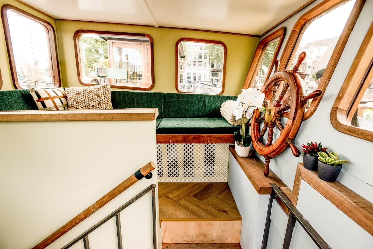 A staircase with a wooden handrail, a green cushioned bench, and a ship's wheel decoration.