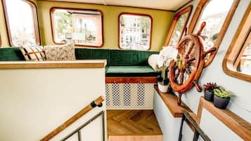 A staircase with a wooden handrail, a green cushioned bench, and a ship's wheel decoration.