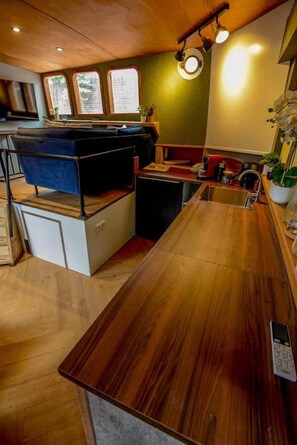 A modern kitchen with a wooden countertop, a built-in seating area, and a view of the outdoors through large windows. - Luxurious boutique houseboat - Deckhouse Suite (Amsterdam)