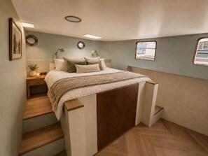 A bedroom with a bed, bedside tables, a nightstand, a lamp, a window, and a staircase.