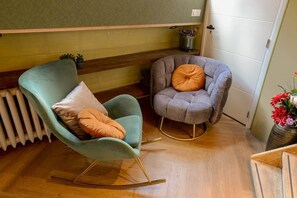 A room with a rocking chair, a cushioned armchair, a radiator, and a potted plant.