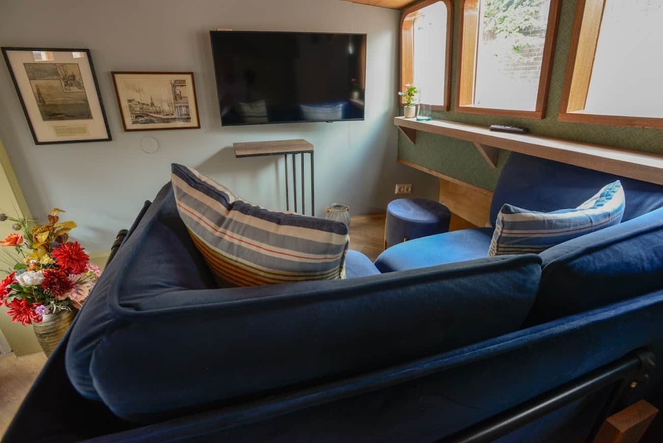 Een gezellig interieur met een bank, een flatscreen televisie, ingelijste foto’s en een tafeltje met een bloevas.