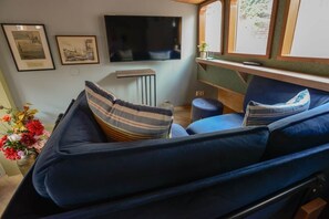 A cozy interior with a sofa, a flat-screen TV, framed pictures, and a small table with a vase of flowers. - Luxurious boutique houseboat - Deckhouse Suite (Amsterdam)