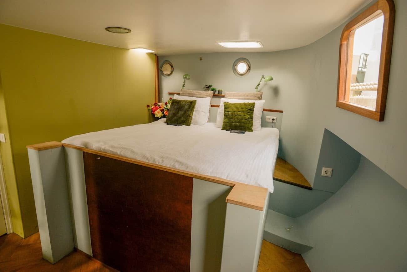 Een slaapkamer met een bed, nachtkastje, raam en een lamp aan de muur.