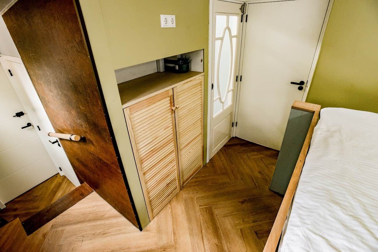 A bedroom with a bed, a wooden wardrobe, and a door leading to another room.