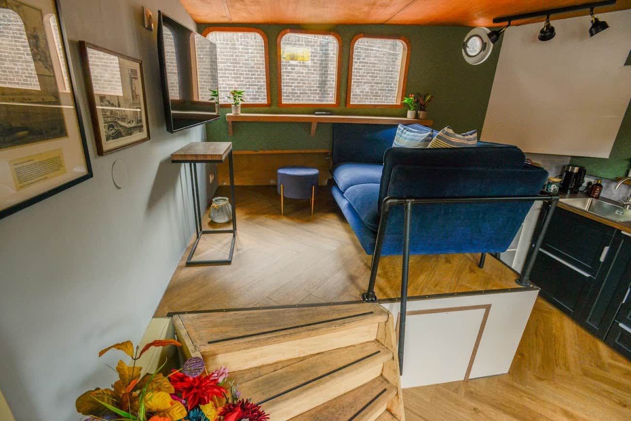 Ett kompakt bostadsutrymme med en soffa, ett litet bord, en trappa och ett köksområde.