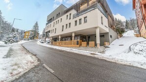 Ein modernes Hotel mit überdachter Einfahrt, einer schneebedeckten Straße und blauem Himmel.