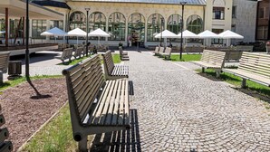 A paved walkway with benches and umbrellas, a building with arched windows, and a clock tower. - Janský Potok II. by Interhome (Janské Lázně)
