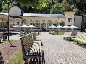 A paved walkway with benches and umbrellas, a building with arched windows, and a clock tower. - Janský Potok II. by Interhome (Janské Lázně)