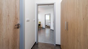 Un pasillo con puertas de madera, un baño a la vista con una cama y un comedor con una silla.