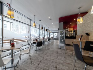 Ein modernes Restaurant mit einer langen Theke, mehreren Tischen und hängenden Pendelleuchten.