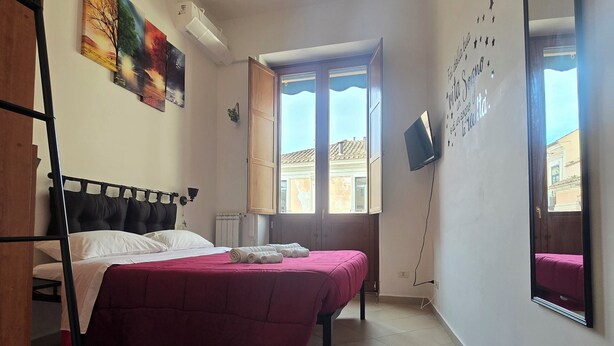 A bedroom with a bed, a window, a radiator, a wall-mounted TV, and a mirror. - BROTHER'S HOUSE APARTMENT (Salerno)