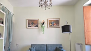 A living room with a sofa, a coffee table, two framed artworks, a hanging plant, a floor lamp, and a radiator. - BROTHER'S HOUSE APARTMENT (Salerno)