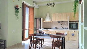 A kitchen with wooden cabinets, a refrigerator, an oven, and a dining area with chairs and a table. - BROTHER'S HOUSE APARTMENT (Salerno)