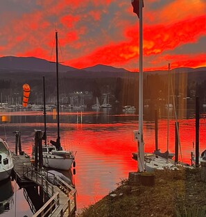 Un port de plaisance avec des bateaux amarrés, un ciel dégagé et des montagnes en arrière-plan.