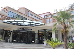 Entrada de un hotel con una cubierta de vidrio, un letrero que dice 'HOTEL TAMGOUT' y una escalera que conduce a la entrada.