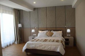 Una habitación de hotel moderna con una cama grande, dos mesitas de noche y una decoración en tonos neutros.
