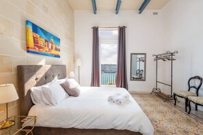 Ein Hotelzimmer mit Bett, einem Bild, einem Fenster mit Vorhängen, einem Kleiderständer und einem Sessel.