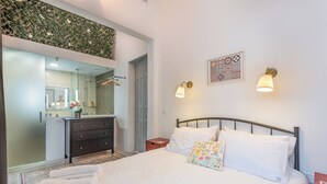 A bedroom with a bed, a dresser, a nightstand, a mirror, and a wall-mounted light fixture. - Regina Suite: 2-bed, 2 en-suite apartment in Valletta with AC and comfort (Valletta)