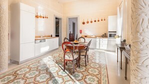 A kitchen with white cabinets, a dining table with chairs, a patterned floor, and hanging kitchen utensils. - Regina Suite: 2-bed, 2 en-suite apartment in Valletta with AC and comfort (Valletta)