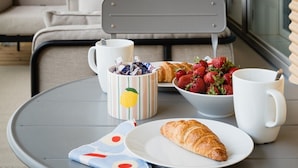 A dining area with a table set for breakfast, including croissants, strawberries, and a coffee mug. - Large 3BR • Sauna • Free Parking • Walk to ferries (Helsinki)