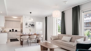 A modern living room with a sofa, coffee table, and dining area with chairs. - Large 3BR • Sauna • Free Parking • Walk to ferries (Helsinki)