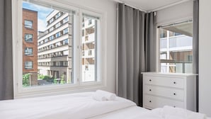 A hotel room with a large bed, a dresser, and a view of a building through the window. - Large 3BR • Sauna • Free Parking • Walk to ferries (Helsinki)